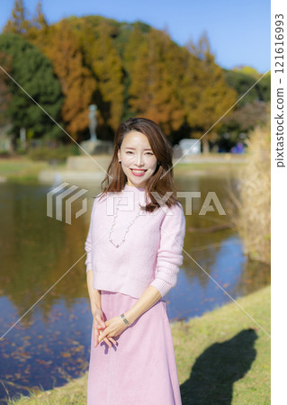 在秋天晴朗的天空下，一位美麗的女士站在水邊。 121616993