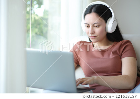 Asian woman wearing headphone using laptop at home Asian woman wearing headphone using laptop at home 121618157