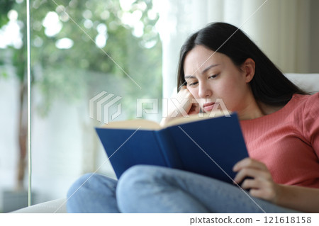 Bored asian woman reading paper book on a couch Bored asian woman reading paper book on a couch 121618158