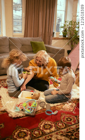 Grandmother engaging with children during medical role-play, supporting knowledge development about treatments and healthy habits. 121618389