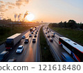 Heavy traffic on a highway during the golden hour of sunrise. Cars, trucks, and a bus move along the road, with a factory emitting smoke in the background. Themes of commuting, transportation, 121618480