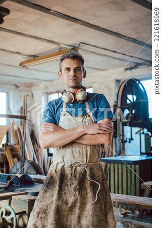 Carpenter standing in his wood workshop looking at camera Carpenter standing in his wood workshop looking at camera 121618969