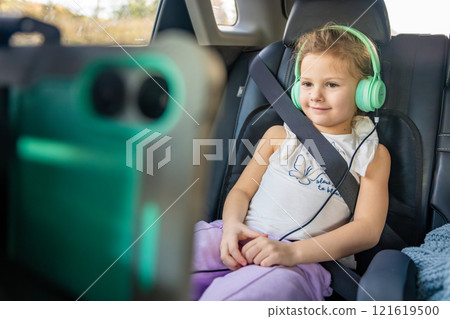 Little girl with tablet and headphones in the car during travel on vacation. Entertainment in the transport for child Little girl with tablet and headphones in the car during travel on vacation. Entertainment in the transport for child 121619500