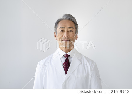 A man in his 60s wearing a white coat looking at the camera 121619940