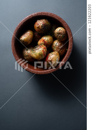 roasted potatoes with herbs and spice in clay bowl on black background, top view roasted potatoes with herbs and spice in clay bowl on black background, top view 121622203
