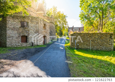A quiet road leads to a historic lime kiln near Kovarska, surrounded by lush greenery and remnants of stone buildings, showcasing the area's industrial heritage in Czechia. 121622763