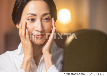 A middle-aged woman doing skin care in the living room at night A middle-aged woman doing skin care in the living room at night 121624312