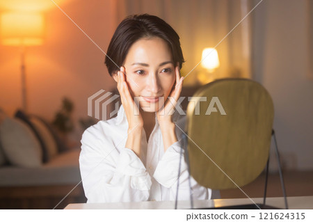 A middle-aged woman doing skin care in the living room at night 121624315