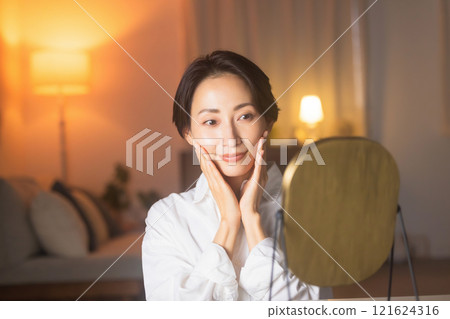 A middle-aged woman doing skin care in the living room at night A middle-aged woman doing skin care in the living room at night 121624316
