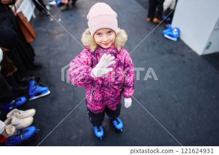 Smiling child waves in colorful winter outfit at ice skating rink 121624931