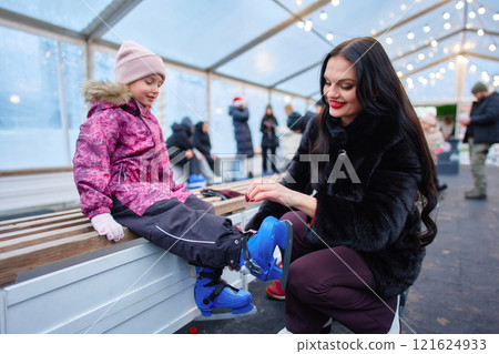 Skating preparation with a young girl in a festive outdoor rink 121624933