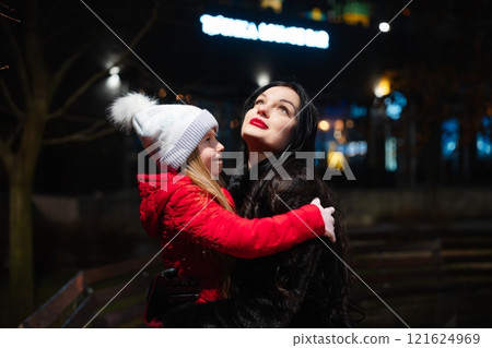 Smiling mother and daughter enjoy the winter evening in a festive urban park surrounded by lights Smiling mother and daughter enjoy the winter evening in a festive urban park surrounded by lights 121624969