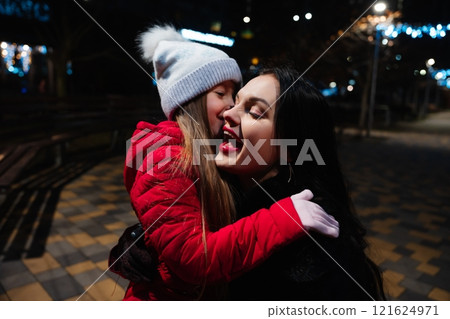 Mother and daughter share a joyful moment in a festive city park at night during winter Mother and daughter share a joyful moment in a festive city park at night during winter 121624971