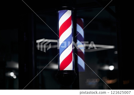 Barber pole with red, white, and blue stripes illuminated at night 121625007