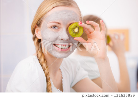 Happy young woman having face mask holding kiwi Happy young woman having face mask holding kiwi 121625959