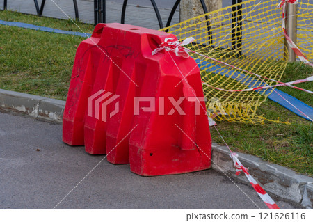 A striking red barrier stands guard on a city street, surrounded by yellow construction netting. Caution tape flutters gently in the breeze, alerting pedestrians to the ongoing work nearby A striking red barrier stands guard on a city street, surrounded by yellow construction netting. Caution tape flutters gently in the breeze, alerting pedestrians to the ongoing work nearby 121626116