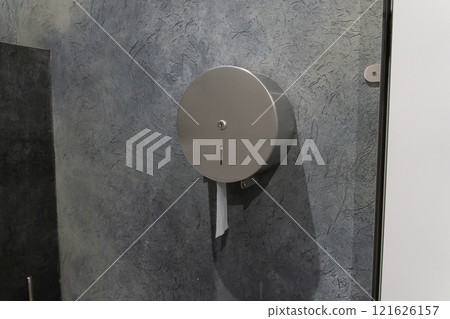 A modern restroom features a round silver paper dispenser affixed to a blue textured wall. This practical fixture is designed for easy access and convenience for users A modern restroom features a round silver paper dispenser affixed to a blue textured wall. This practical fixture is designed for easy access and convenience for users 121626157