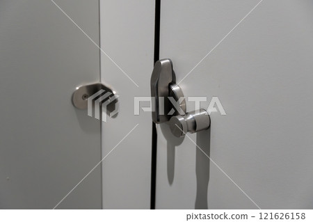 A pair of sleek stainless steel locks are fastened to a white cabinet door, highlighting the modern design elements of the interior space A pair of sleek stainless steel locks are fastened to a white cabinet door, highlighting the modern design elements of the interior space 121626158