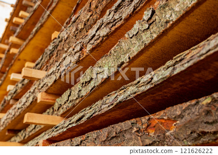 Timber planks are neatly stacked and arranged in a sawmill, absorbing the golden sunlight. Their natural textures highlight the craftsmanship involved in logging and lumber production 121626222