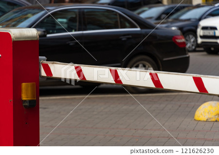 A bright red barrier stands at the entrance of a busy parking lot, preventing entry while vehicles wait in line. The scene reflects measures for safety and security in public spaces A bright red barrier stands at the entrance of a busy parking lot, preventing entry while vehicles wait in line. The scene reflects measures for safety and security in public spaces 121626230