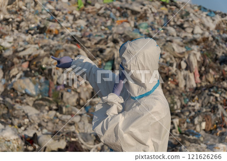 A sanitation worker in protective gear points at a towering mountain of trash at a landfill, highlighting the urgent need for waste management and recycling amid rising pollution concerns 121626266