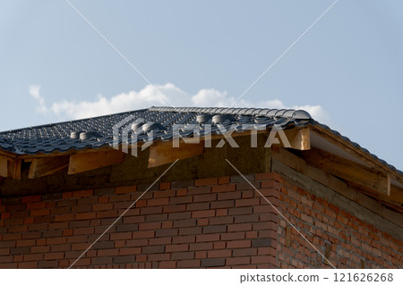 Rooftop features metallic tiles newly installed on a residential home, showcasing a blend of modern architecture and traditional roofing techniques against a clear sky 121626268