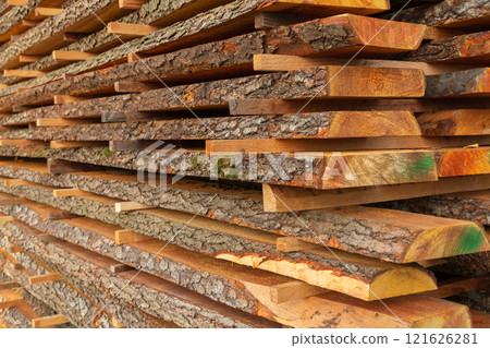 Sturdy timber planks are neatly stacked and dried under bright sunlight at a sawmill. The arrangement highlights the unique textures and vibrant colors of the natural wood 121626281