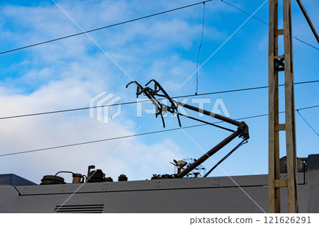 Overhead lines and a pantograph extend from a modern electric train, connecting it to power sources. This illustrates the crucial infrastructure of railway transport Overhead lines and a pantograph extend from a modern electric train, connecting it to power sources. This illustrates the crucial infrastructure of railway transport 121626291