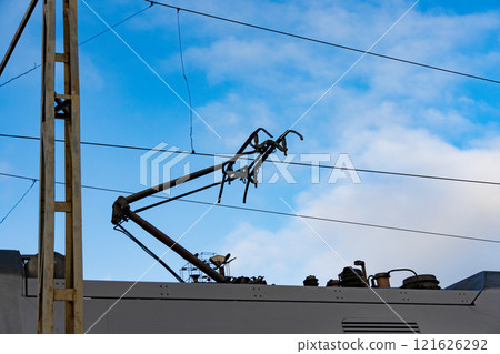 Electric train components are visible against a vibrant blue sky, showcasing the intricate design of modern railway systems and their essential infrastructure 121626292