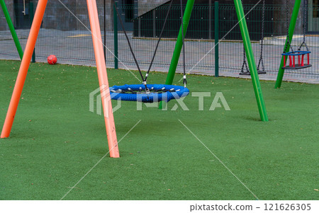 Colorful swings await children in a lively park setting, surrounded by inviting greenery and safe play areas. Kids can indulge in fun and playful activities, enjoying their time outdoors Colorful swings await children in a lively park setting, surrounded by inviting greenery and safe play areas. Kids can indulge in fun and playful activities, enjoying their time outdoors 121626305