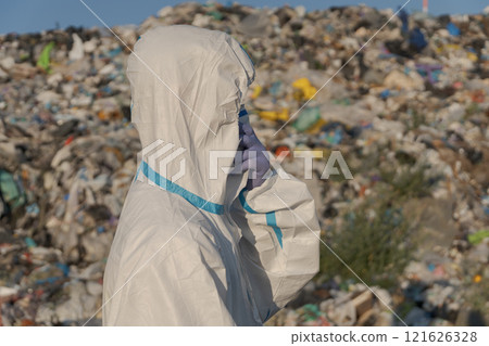 A worker in protective gear surveys a large landfill filled with trash and plastic debris, drawing attention to the pressing issues of pollution and waste management 121626328