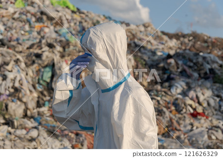 A sanitation worker in protective clothing examines a large landfill overflowing with waste, emphasizing the urgent need for effective waste management and recycling efforts A sanitation worker in protective clothing examines a large landfill overflowing with waste, emphasizing the urgent need for effective waste management and recycling efforts 121626329