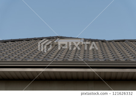 A modern residential roof features sleek metallic tiles with a skylight. The rooftop design blends functionality and aesthetics against a clear blue sky 121626332