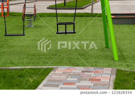 Swings in a vibrant public park invite children to experience the joys of childhood. The green grass and sunny atmosphere enhance the playful environment for outdoor fun Swings in a vibrant public park invite children to experience the joys of childhood. The green grass and sunny atmosphere enhance the playful environment for outdoor fun 121626354