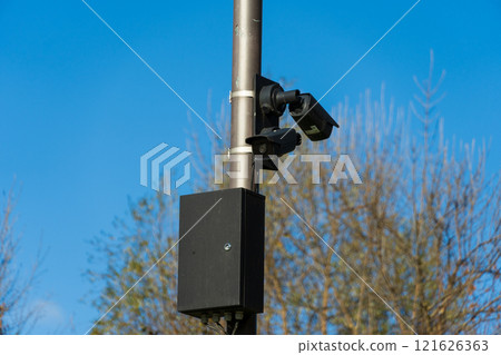 CCTV cameras are securely mounted on metal poles, actively monitoring the surroundings in an outdoor area surrounded by trees, during clear blue sky daylight conditions 121626363