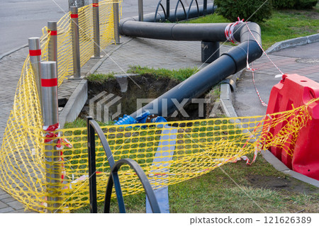 Workers are replacing old water pipes on the street, using digging equipment while ensuring safety with barriers and caution tape around the construction site 121626389