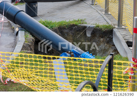 Workers are engaged in replacing water pipes on the street, utilizing heavy machinery to dig and install new pipelines amidst construction hazards and safety barriers 121626390