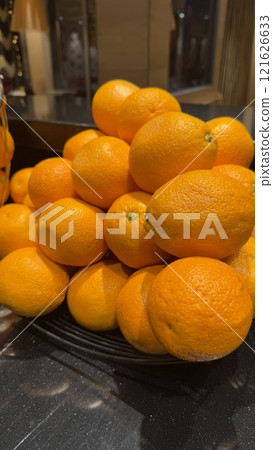 Stack of Vibrant Fresh Oranges Displayed in a Basket on a Dark Counter Stack of Vibrant Fresh Oranges Displayed in a Basket on a Dark Counter 121626633