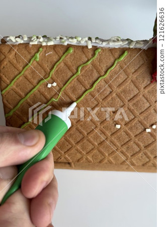Decorating a Gingerbread House With Green Icing for Holiday Celebration Decorating a Gingerbread House With Green Icing for Holiday Celebration 121626636