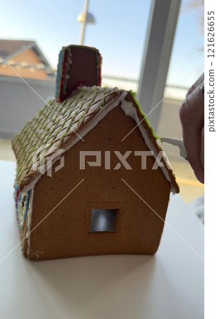 Decorating Gingerbread House Roof with Icing in a Festive Setting Decorating Gingerbread House Roof with Icing in a Festive Setting 121626655