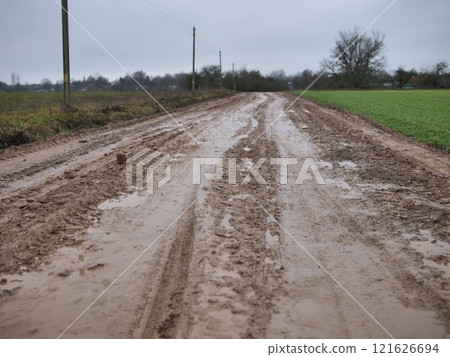 A wet and muddy rural road is visible, showcasing tire tracks and puddles, all beneath a cloudy sky above A wet and muddy rural road is visible, showcasing tire tracks and puddles, all beneath a cloudy sky above 121626694