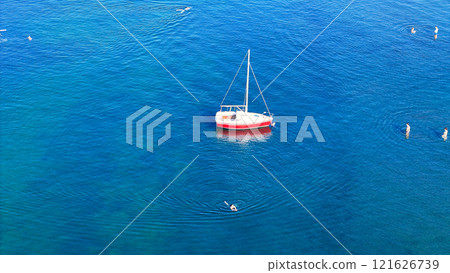 Sailboat floating on calm blue water with people swimming nearby 121626739
