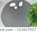 A stylish and contemporary round grey rug enriched with stones and accompanied by a green plant. Summer holiday concept  121627027