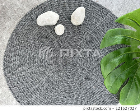 A stylish and contemporary round grey rug enriched with stones and accompanied by a green plant. Summer holiday concept  121627027