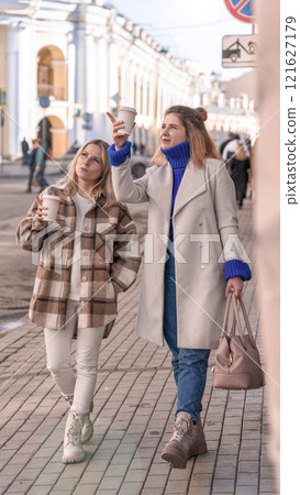 two young girls are walking along the city street, drinking coffee, talking two young girls are walking along the city street, drinking coffee, talking 121627179