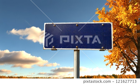 A deserted signboard stands proudly under a clear blue sky, surrounded by golden autumn foliage. The emptiness sparks curiosity about its purpose.  121627713