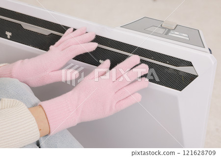 Frozen young woman in mittens warming near radiator at home, closeup. Frozen young woman in mittens warming near radiator at home, closeup. 121628709