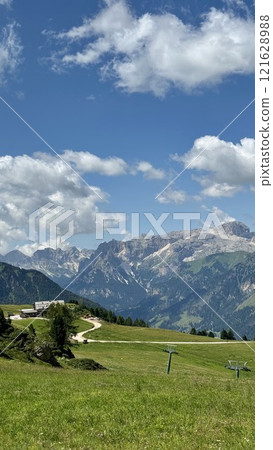 Scenic Mountain Landscape with Sunny Blue Sky and Rolling Green Fields in Dolomites, Italy Scenic Mountain Landscape with Sunny Blue Sky and Rolling Green Fields in Dolomites, Italy 121628988
