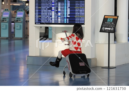 A tourist moving through the airport lobby straddling a carry-on bag A tourist moving through the airport lobby straddling a carry-on bag 121631730