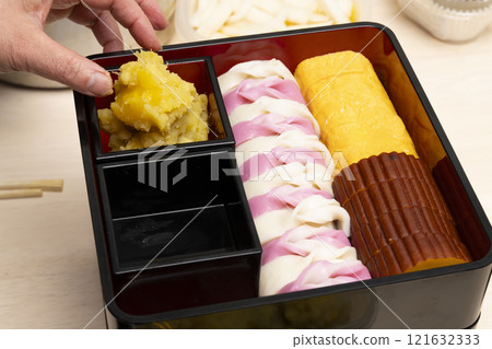 Packing New Year's food into a tiered box with chopsticks Packing New Year's food into a tiered box with chopsticks 121632333
